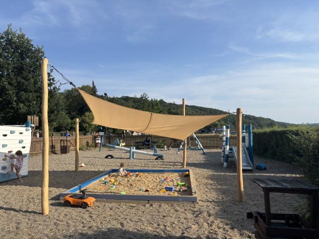 Pískoviště pod stínící plachtou na hřišti, vedle houpačky a skluzavka