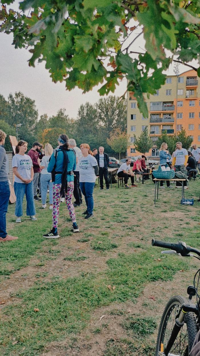 Kandidáti v tričkách s nápisem Jdeme za vámi a první návštěvníci se scházejí na trávníku u domů