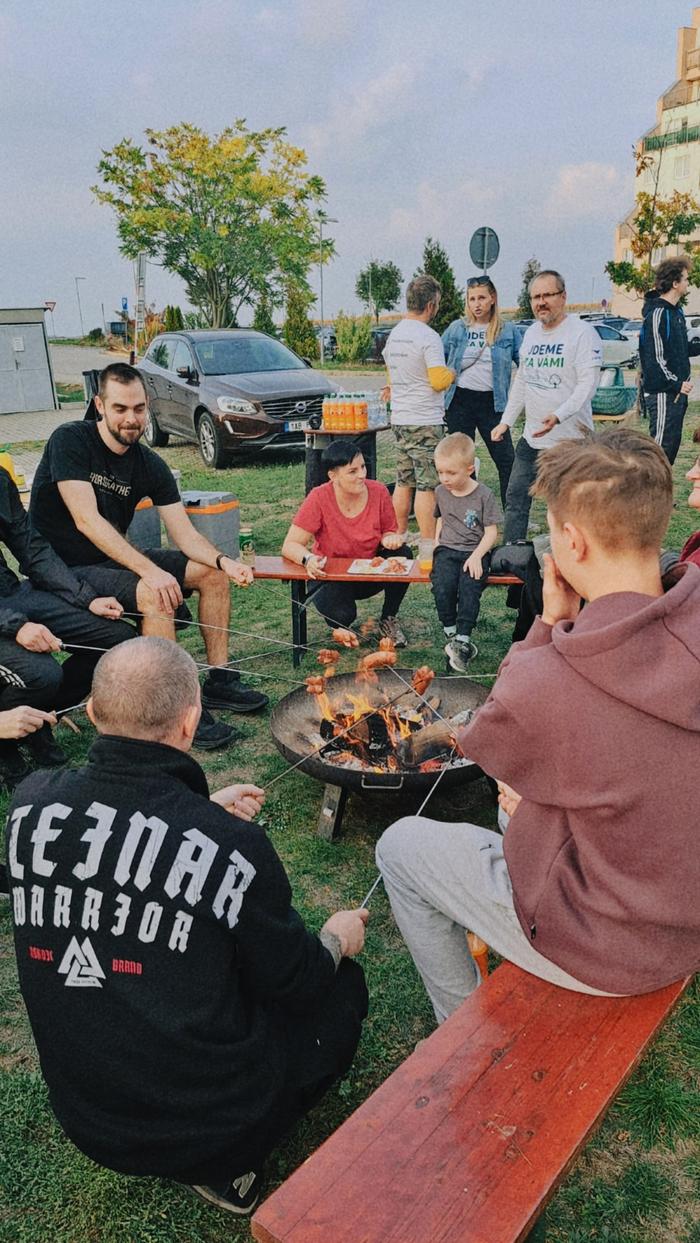 Skupina lidí opéká buřty nad ohništěm