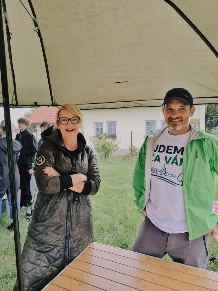 Žena a muž v tričku s nápisem Jdeme za vámi pod přístřeškem