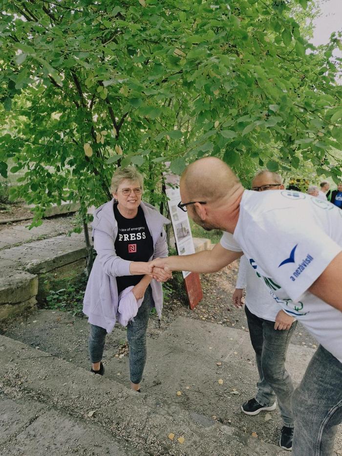 Muž v tričku s nápisem Jdeme za vámi vítá příchozí podáním ruky