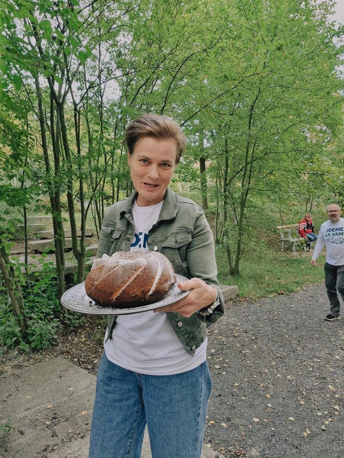 Žena nese na podnose bábovku po lesní cestě