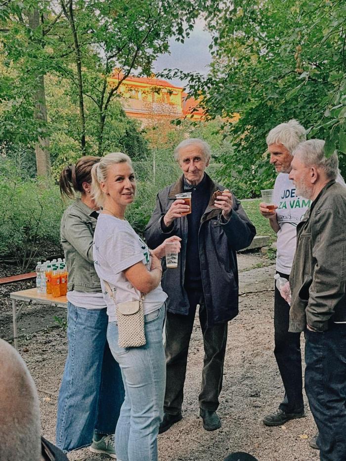 Skupina lidí s nápoji rozmlouvá pod stromy