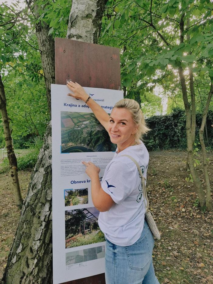 Žena upravuje informační panel opřený o břízu