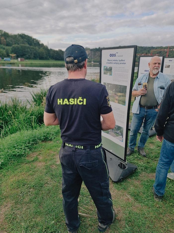 Muž v tričku s nápisem Hasiči si čte informační panel