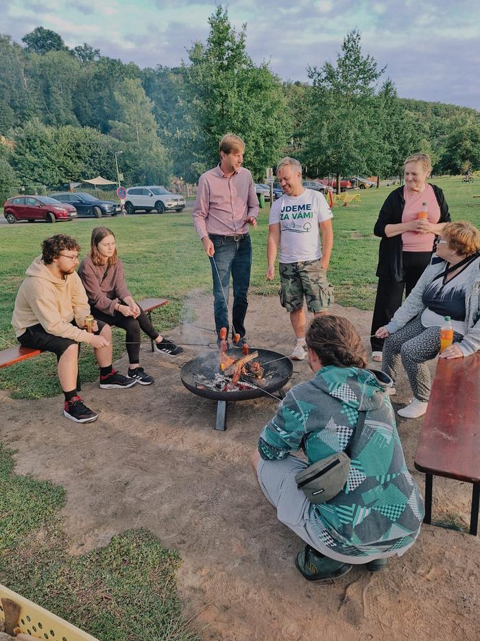 Lidé stojí a sedí kolem ohniště